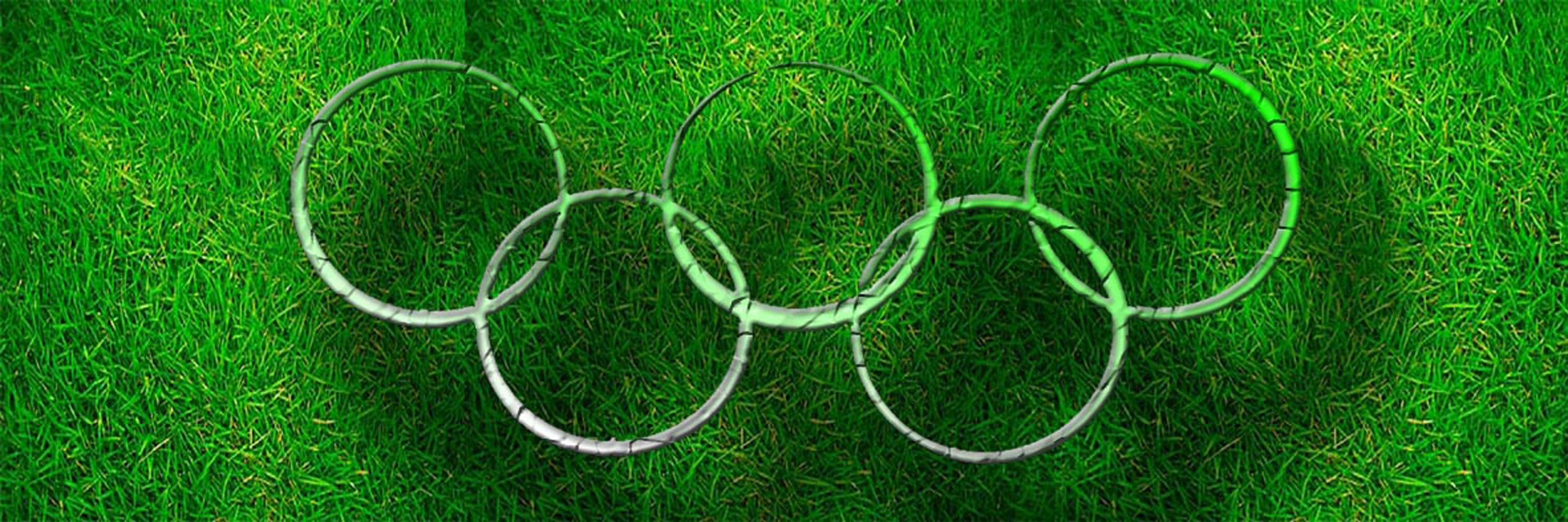 Cornice composta da i cinque anelli olimpici concatenati sullo sfondo di un prato verde 